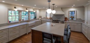 View of a brand new kitchen with huge island, grey cabinetry, marble countertops, a farmhouse sink, and gold fixtures.
