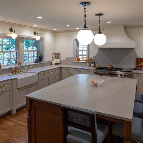 View of a brand new kitchen with huge island, grey cabinetry, marble countertops, a farmhouse sink, and gold fixtures.
