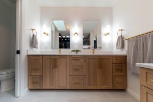 View of the double vanity in a newly remodeled master bathroom with a walk-in black shower and gold finishes.