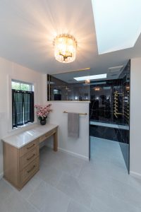 View of the makeup vanity in a newly remodeled master bathroom with a walk-in black shower and gold finishes.