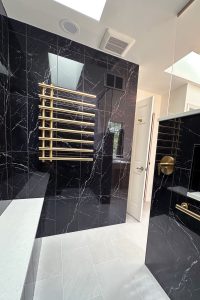 Close up view of the heated towel bars in a walk-in shower with black tile, gold fixtures, and a hidden drain.