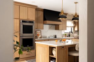 Remodeled kitchen with a large island, warm cabinetry, and black and gold accents.